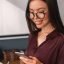 cheerful-female-executive-in-glasses-reading-her-messages-on-mobile-phone-with-note-book-in-hands.jpg